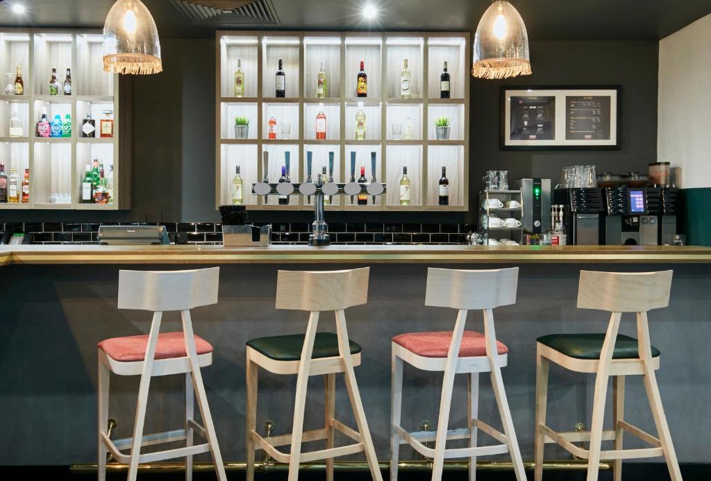 a bar with four stools in front of a counter at Leonardo Hotel Manchester Central in Manchester