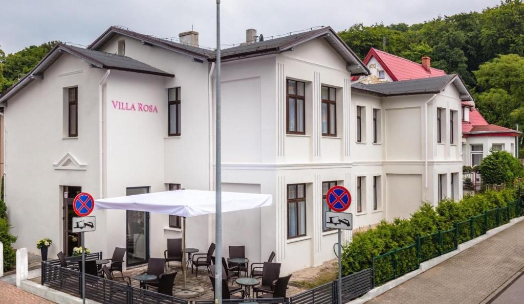 ein weißes Gebäude mit Stühlen und einem Sonnenschirm davor in der Unterkunft Villa Rosa - 200m od morza in Misdroy