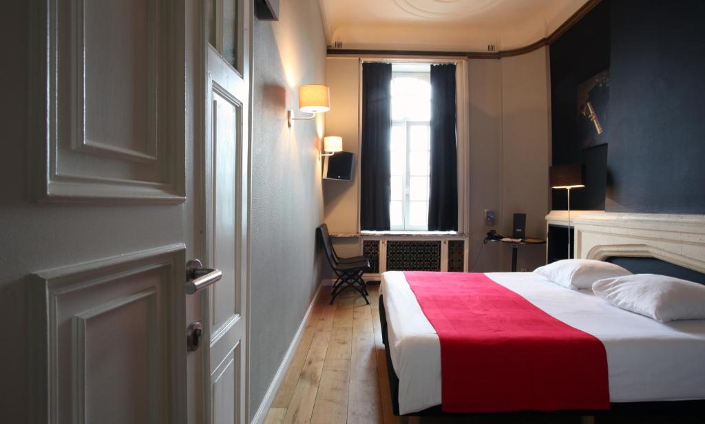 een slaapkamer met een bed met een rode deken en een raam bij Hotel La Royale in Leuven