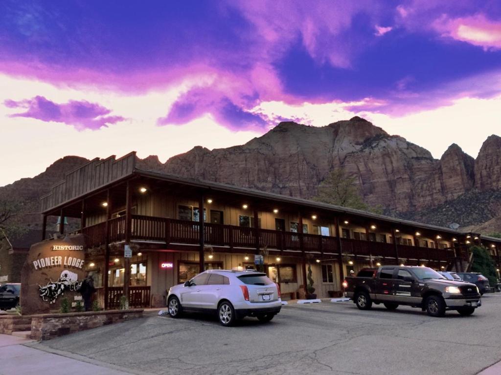a building with cars parked in a parking lot with mountains at Pioneer Lodge Zion National Park-Springdale in Springdale