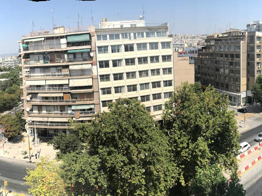 een hoog wit gebouw met bomen voor een straat bij Hotel Rex in Thessaloniki