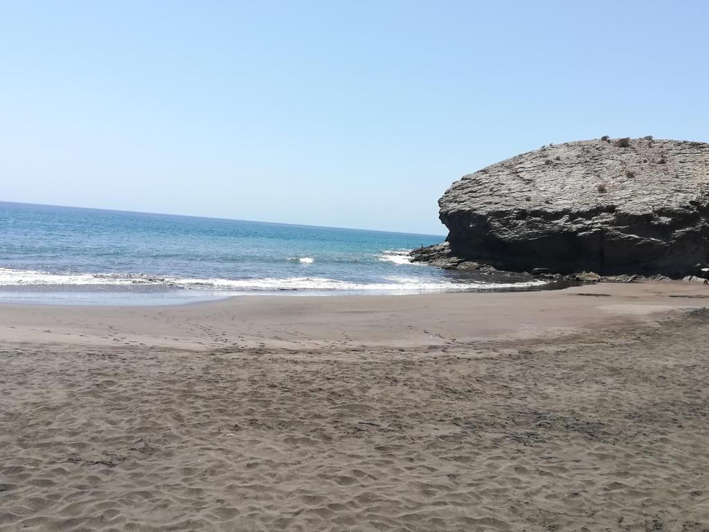 a sandy beach with a large rock in the ocean at Casa El Pino in Mogán