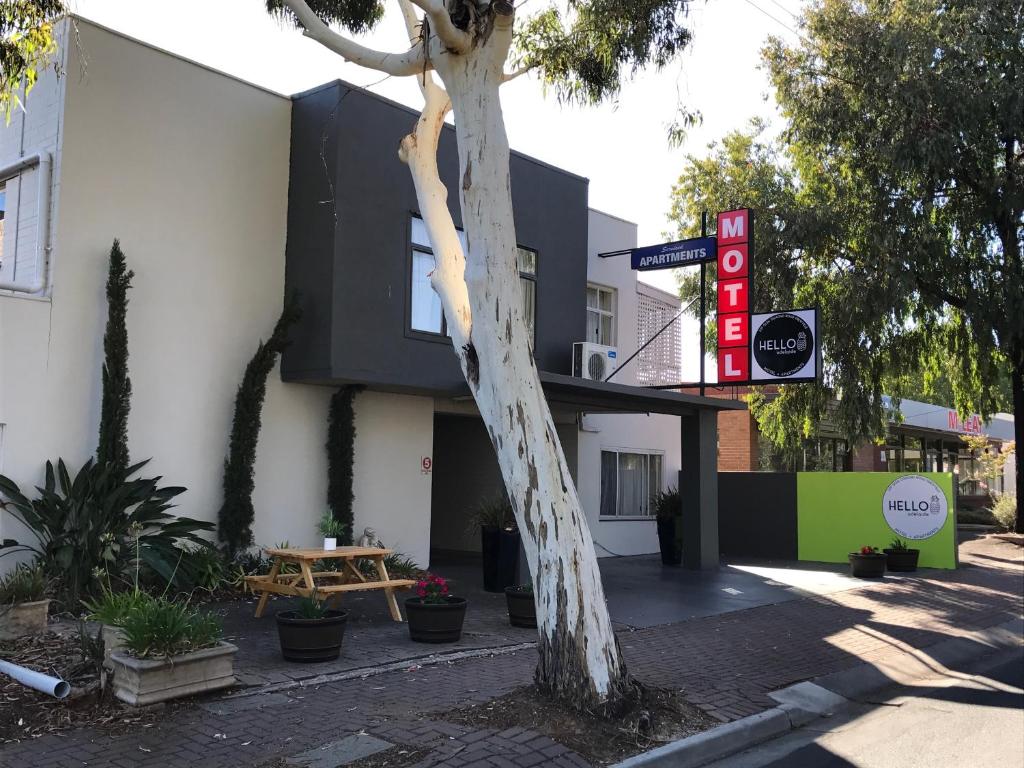 a tree in front of a building with a sign at Hello Adelaide Motel and Apartments in Adelaide