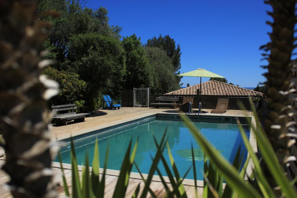 a swimming pool with a patio and an umbrella at La Poussada, maisons écologiques avec vue mer in Lapalme