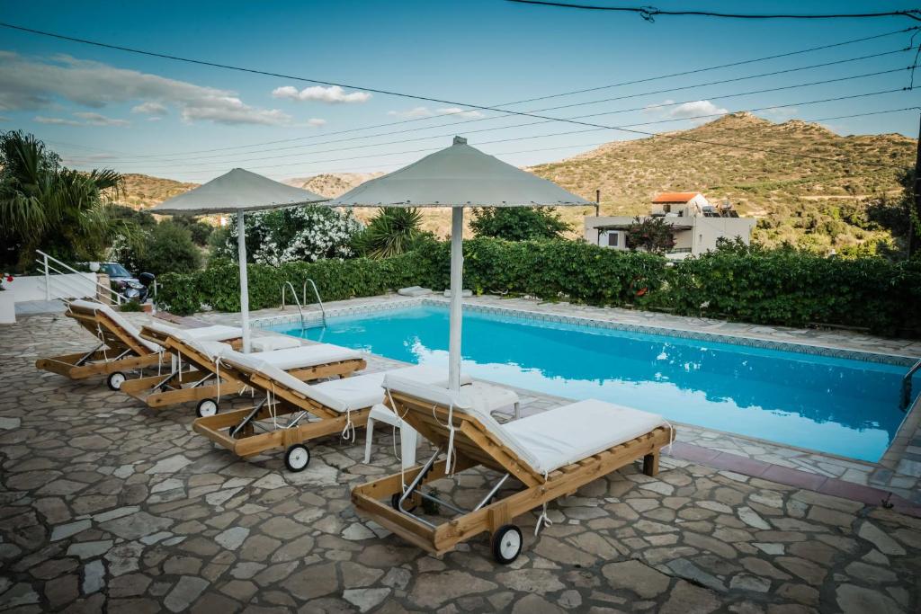 een groep ligstoelen en parasols naast een zwembad bij Marina Hotel in Matala