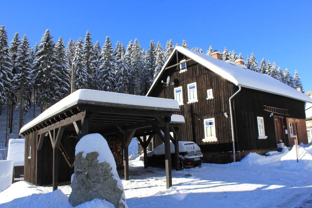 a barn with a snow covered roof in front of trees at Ferienhaus Anno Dazumal, wie zu Oma`s Zeiten in Klingenthal