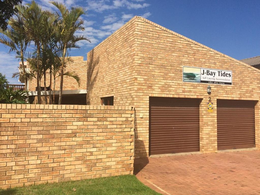 a brick building with two garage doors and a sign at Jbay Tides in Jeffreys Bay