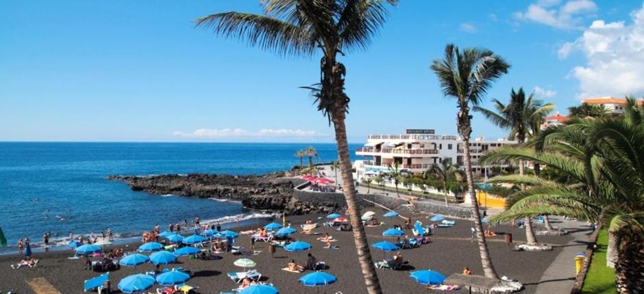einen Strand mit Palmen und blauen Sonnenschirmen und dem Meer in der Unterkunft Apartamento Avenida in Puerto de Santiago
