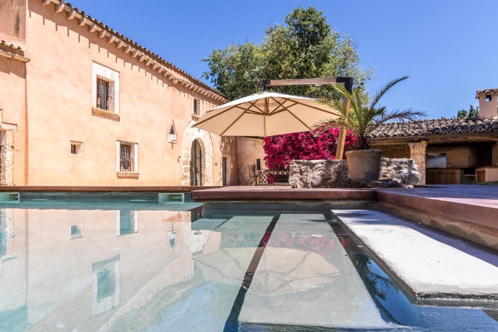 a swimming pool with an umbrella next to a building at Villa Florit in Búger