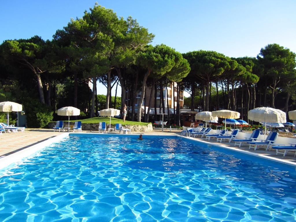 una gran piscina con sillas azules y árboles en Hotel Beau Rivage Pineta, en Lido di Jesolo