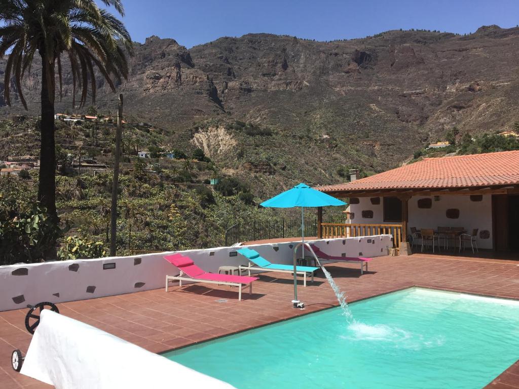 a swimming pool with an umbrella and a house at Casa Rural Tadia in San Bartolomé