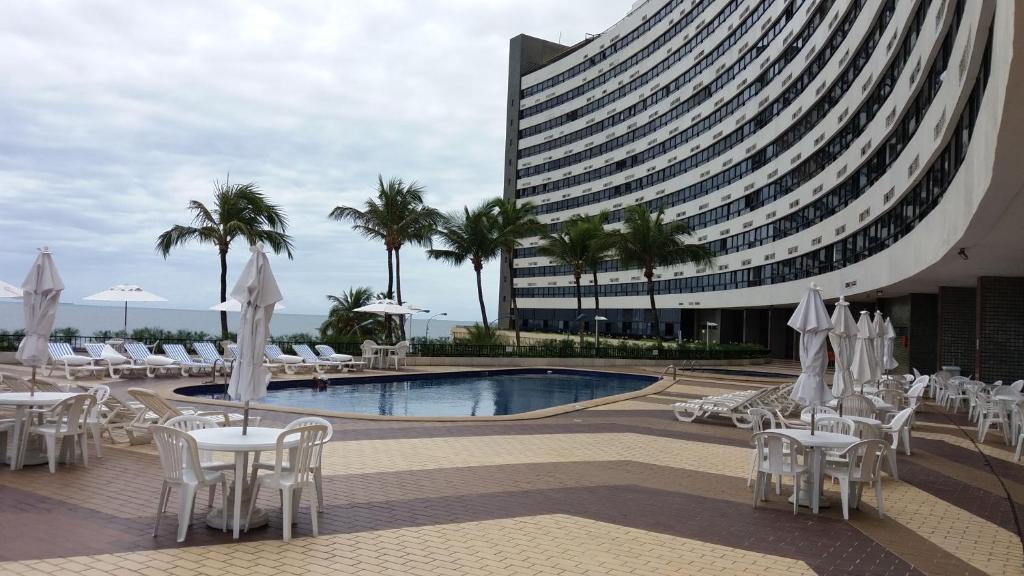 uma piscina com mesas e cadeiras brancas e um edifício em Apart Hotel em Ondina em Salvador