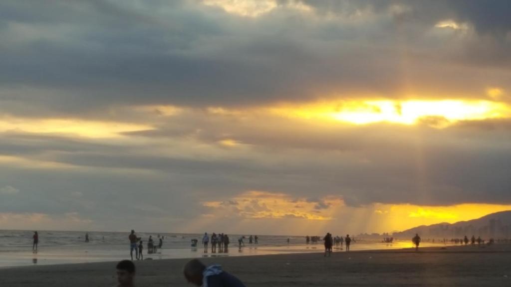 eine Gruppe von Menschen am Strand bei Sonnenuntergang in der Unterkunft Vista para o Mar Praia Grande in Praia Grande