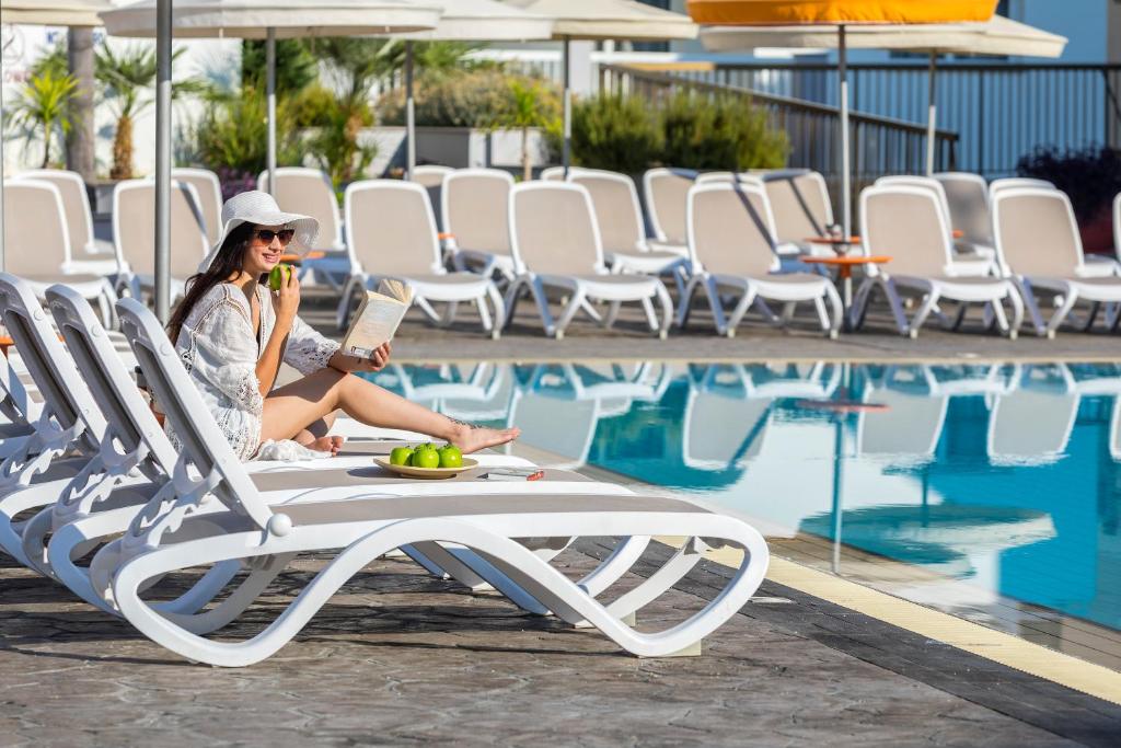 uma mulher sentada numa espreguiçadeira a ler um livro à beira da piscina em Christabelle Hotel Apartments em Agia Napa