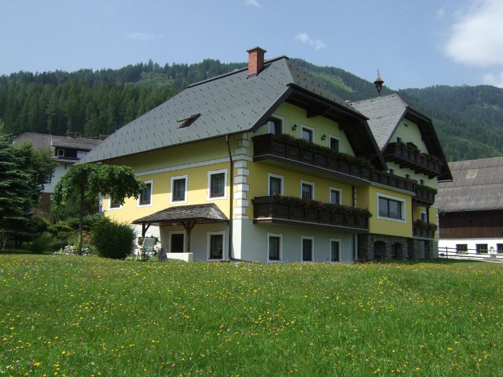 une grande maison jaune dans un champ d'herbe dans l'établissement Ferienwohnungen Trattner, à Mauterndorf