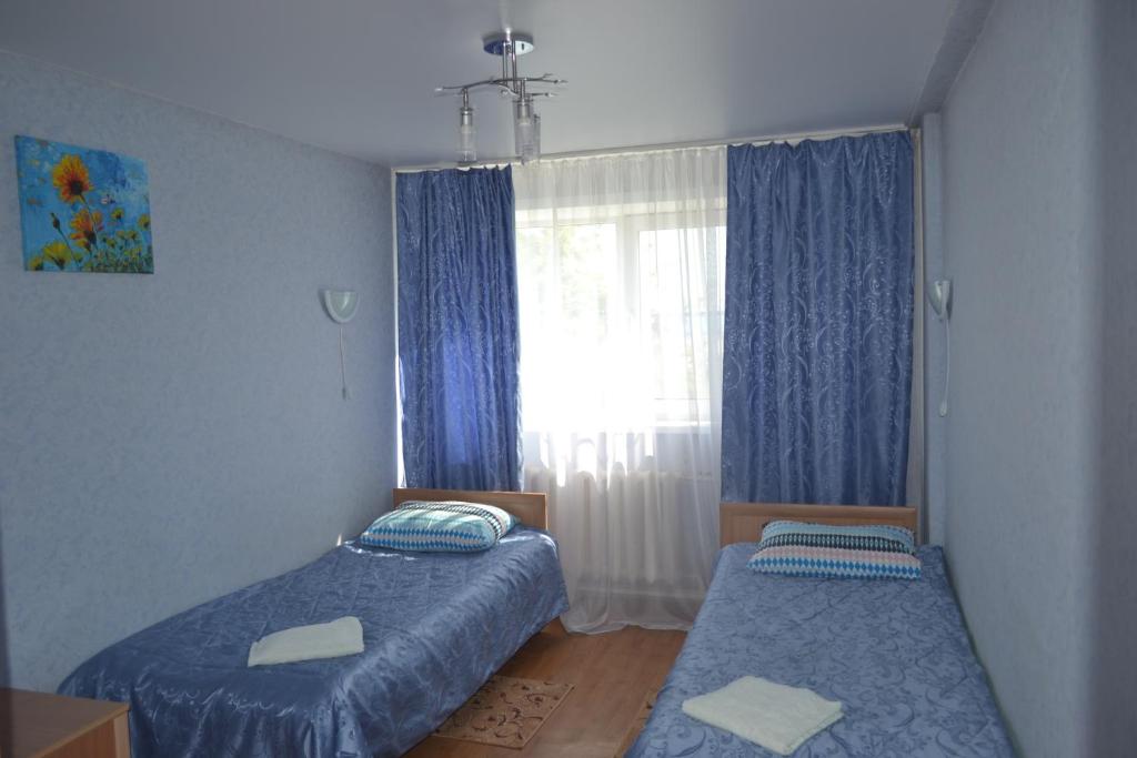 a bedroom with two beds and a window with blue curtains at Hotel Rassvet in Saransk