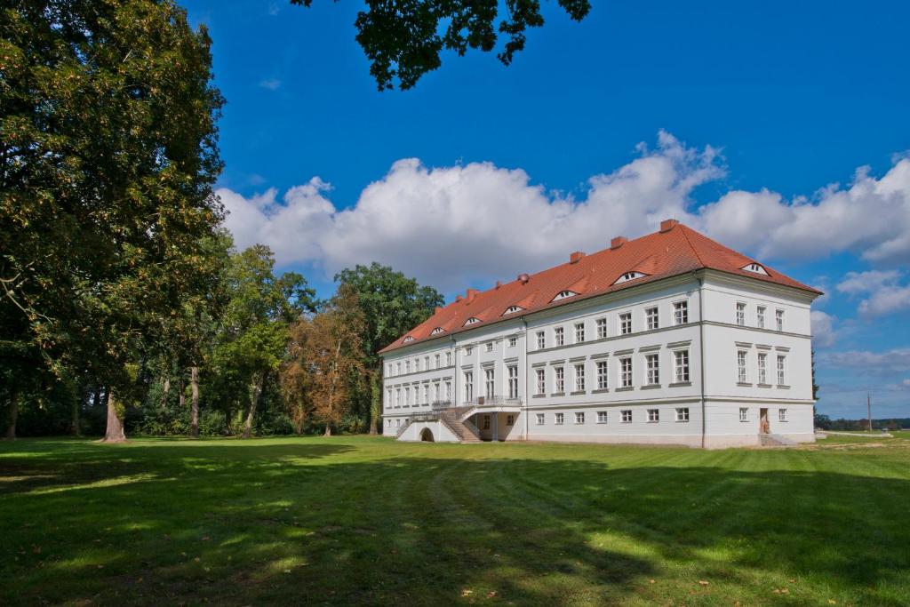 um edifício branco com um telhado vermelho num campo verde em Schloss Retzow Apartments em Retzow