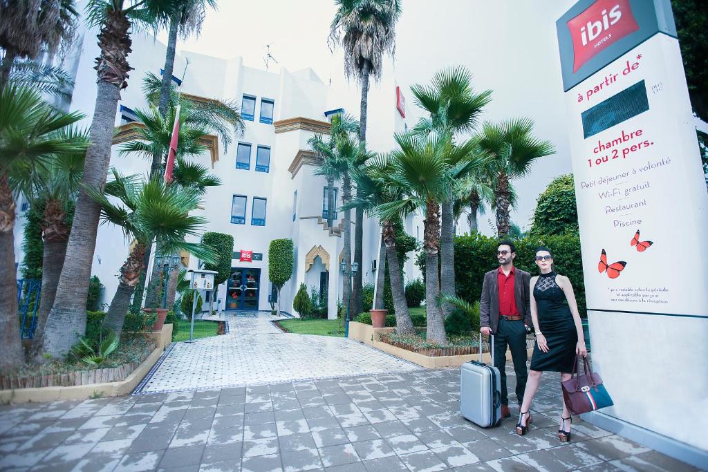 un homme et une femme debout devant un bâtiment avec bagages dans l'établissement Ibis Fes, à Fès