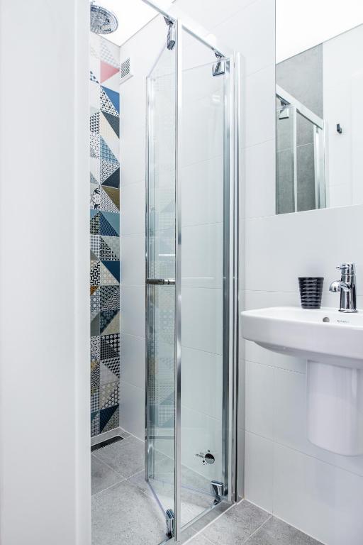 Compact shower cubicle with glass folding door and colorful geometric accent tiles, adjacent white sink