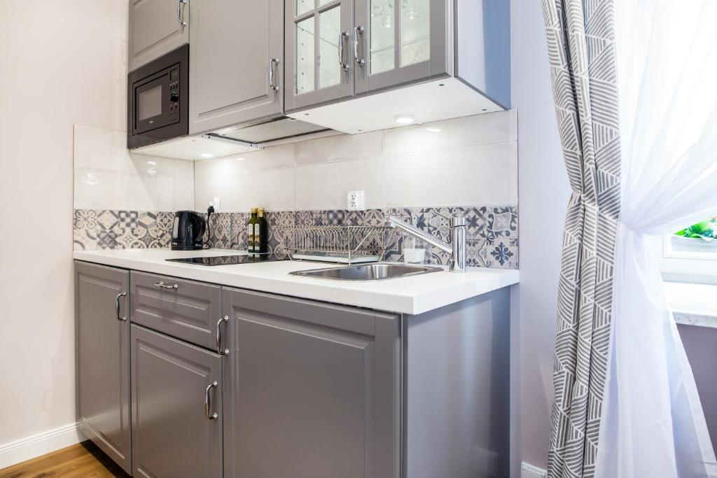 Small kitchenette with gray cabinets, sink, microwave, electric kettle, patterned tile backsplash and window