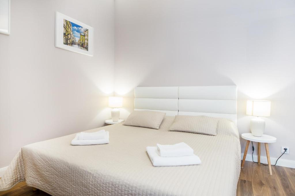 Neutral bedroom with beige quilted double bed, white headboard, bedside lamps and folded towels.