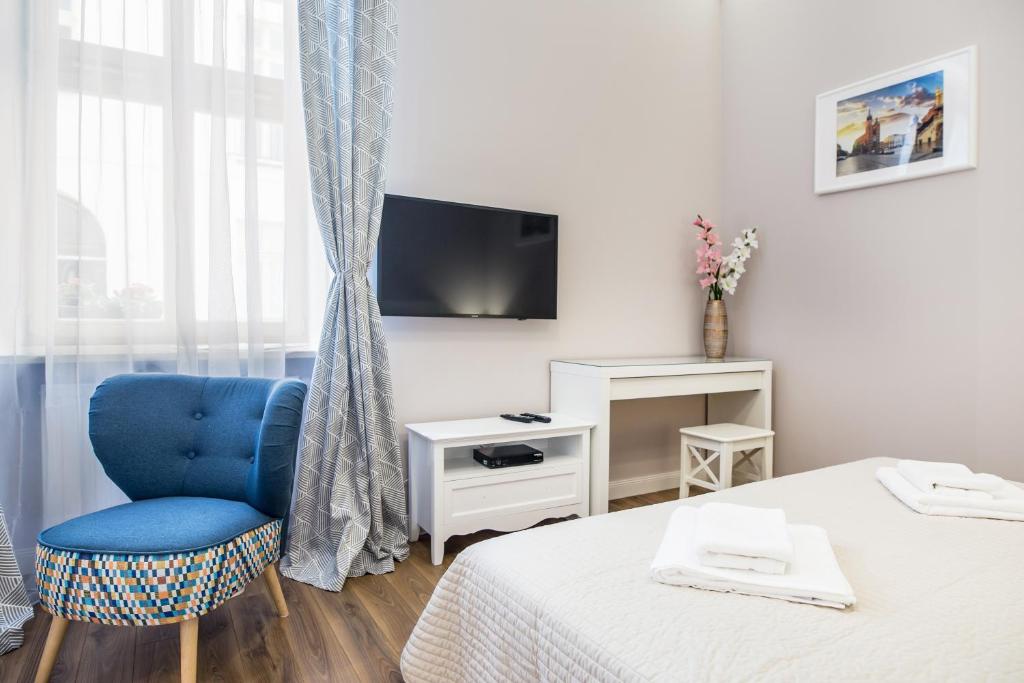 Bright bedroom corner with blue accent chair, wall-mounted TV, white desk and neatly folded towels.