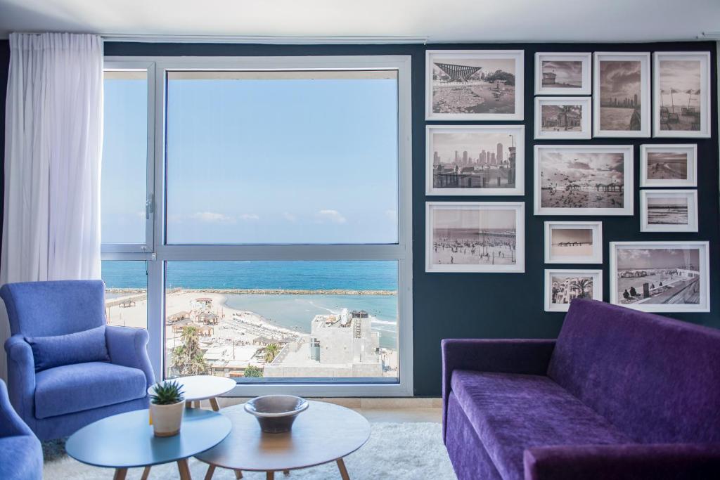 sala de estar con sofá púrpura y ventana grande en Tal By The Beach - An Atlas Boutique Hotel en Tel Aviv