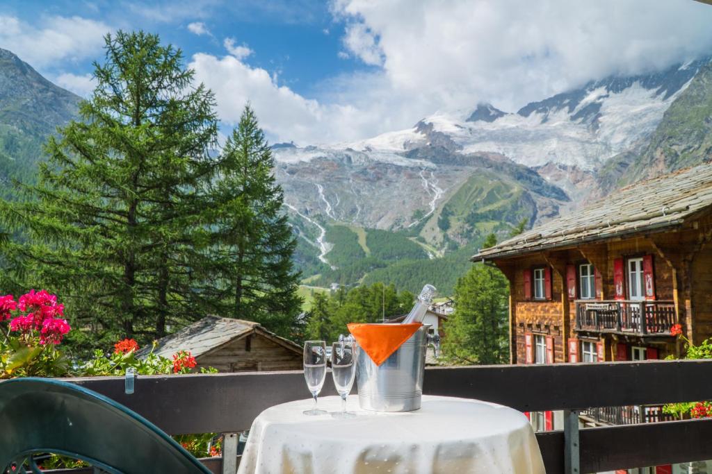 a table with two wine glasses on it with a view of mountains at Hotel La Collina in Saas-Fee