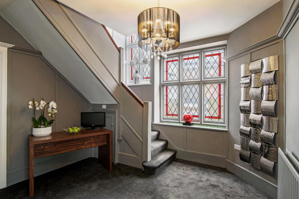 einen Flur mit einer Treppe mit einem Kronleuchter und einem Schreibtisch in der Unterkunft M-Hotels Apartments in London