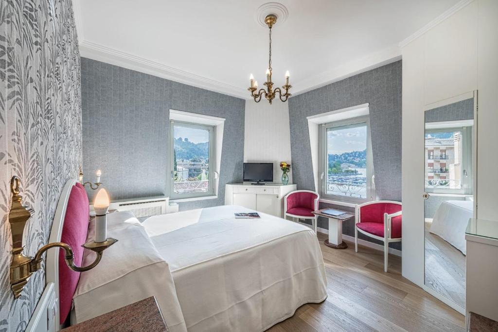 a bedroom with a white bed and two pink chairs at Hotel Metropole Suisse in Como