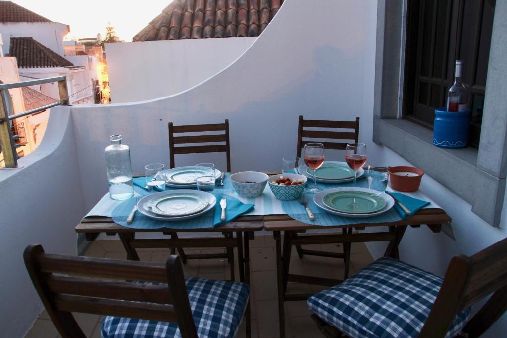 einen Tisch mit Tellern und Weingläsern auf dem Balkon in der Unterkunft Peixe Agulha in Tavira