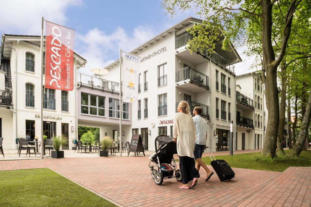 a woman pushing a baby in a stroller in front of a building at AKZENT Apartmenthotel Residenz in Graal-Müritz