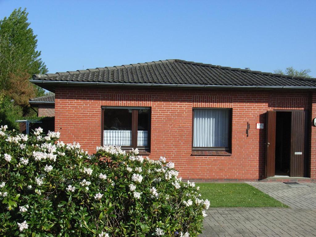 ein rotes Backsteinhaus mit weißen Blumen davor in der Unterkunft Baltrumweg 1 in Wangerland