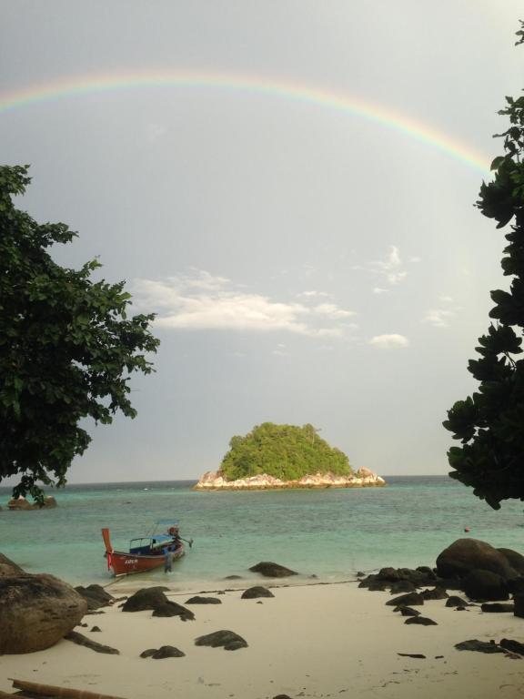a rainbow over a beach with a chair and an island at Kathalee Beach Resort & Spa in Ko Lipe
