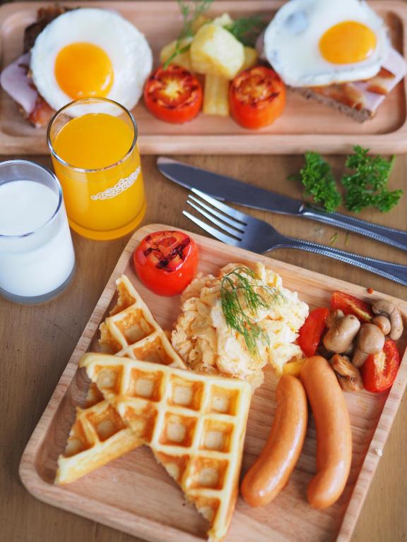 A staged breakfast spread features eggs, waffles, sausages, fruit, juice, and milk.