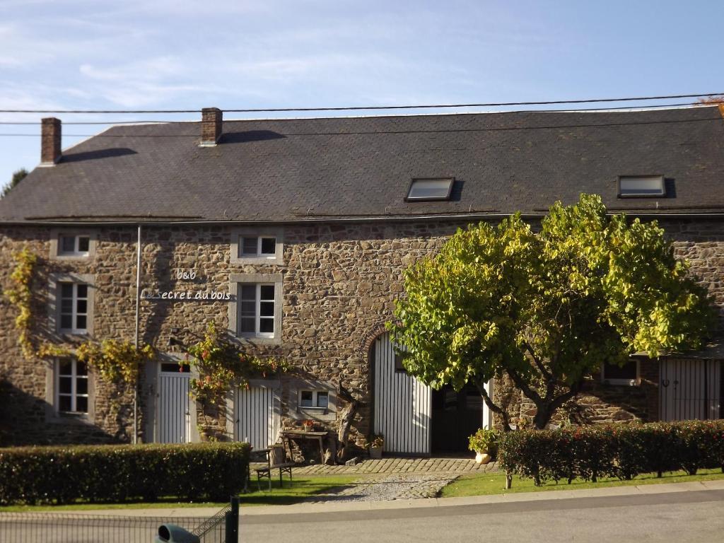 un edificio in pietra con un albero di fronte di B&B Le Secret Du Bois a Bourseigne-Vieille
