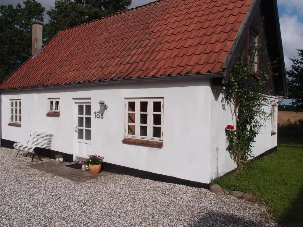 uma pequena casa branca com um telhado vermelho em Bjældskovgaard Holiday House em Funder Kirkeby