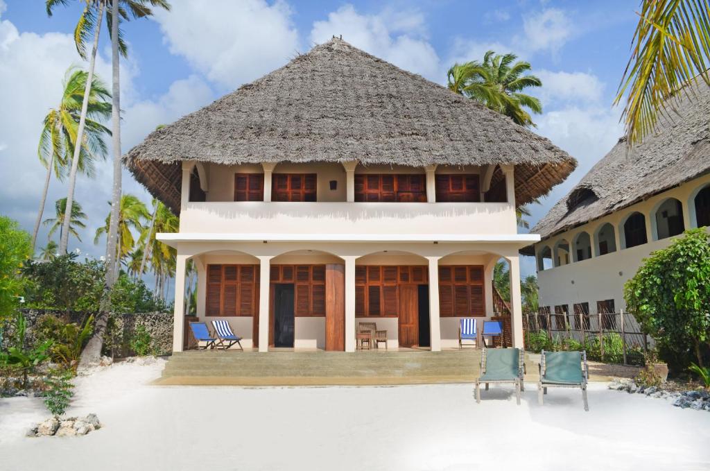 een huis op het strand met stoelen en palmbomen bij Alibi's Well in Jambiani