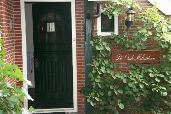 una casa de ladrillo con una puerta verde y un cartel en B&B De Oude Molensteen en Eelde-Paterswolde
