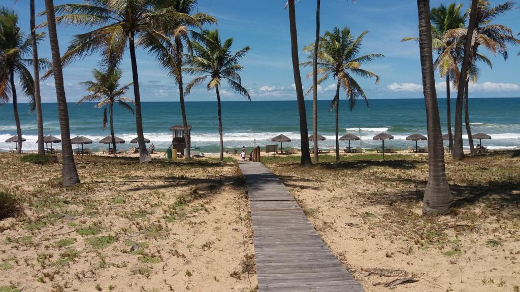 un chemin en bois menant à la plage avec des palmiers et l'océan dans l'établissement Vila dos Lírios -Tranquilidade e Natureza, à Imbassaí