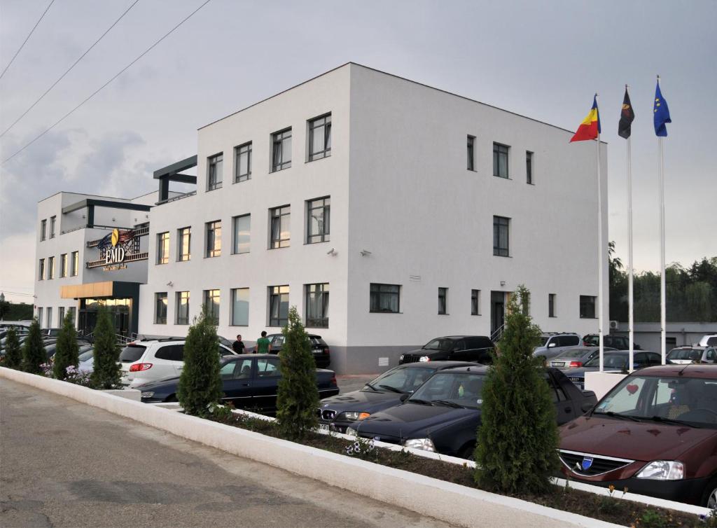 un bâtiment blanc avec des voitures garées dans un parking dans l'établissement Hotel EMD, à Bacău