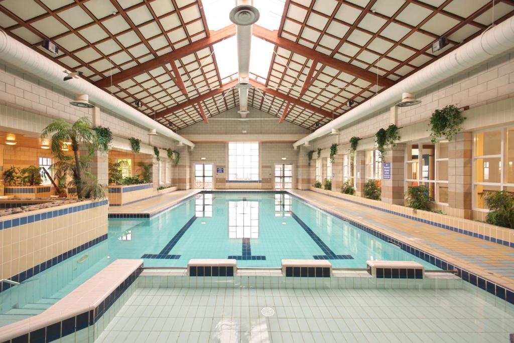 Indoor swimming pool with tiled flooring, large windows, and poolside chairs.