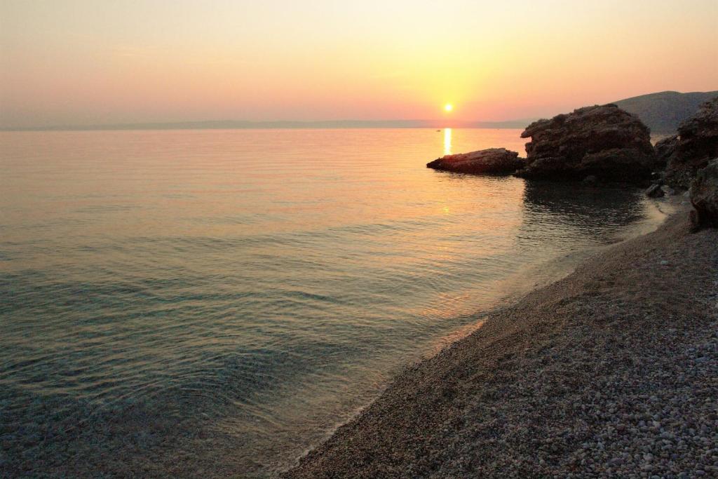 a sunset over the ocean with a rocky beach at Quercus Apartment in Stara Baška