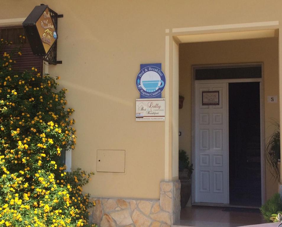 una puerta delantera de una casa con flores amarillas y un cartel en B&B Lolly en Paravati