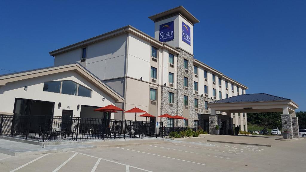 Sleep Inn & Suites Belmont - St. Clairsville في Belmont: مبنى الفندق مع مظلات حمراء في مواقف السيارات