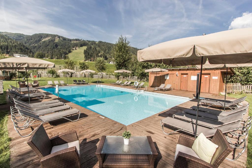 a swimming pool with chairs and an umbrella at Familienresort Reslwirt in Flachau