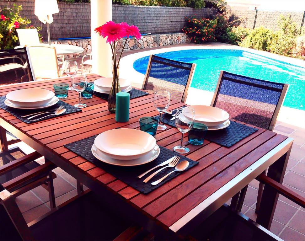a wooden table with plates and wine glasses next to a pool at Villa Son Remei in Punta Prima