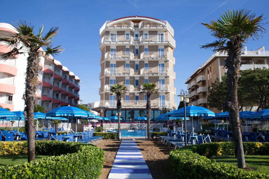 a resort with a pool and palm trees and blue umbrellas at Regent's Hotel in Lido di Jesolo