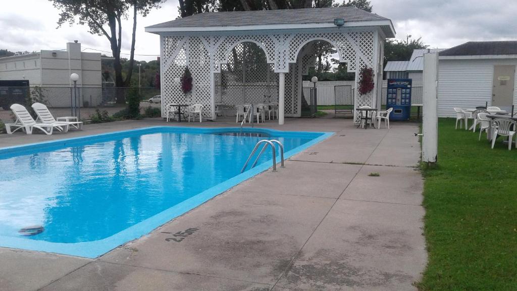 a swimming pool with a gazebo and chairs and tables at Auberge le Parasol in Saguenay