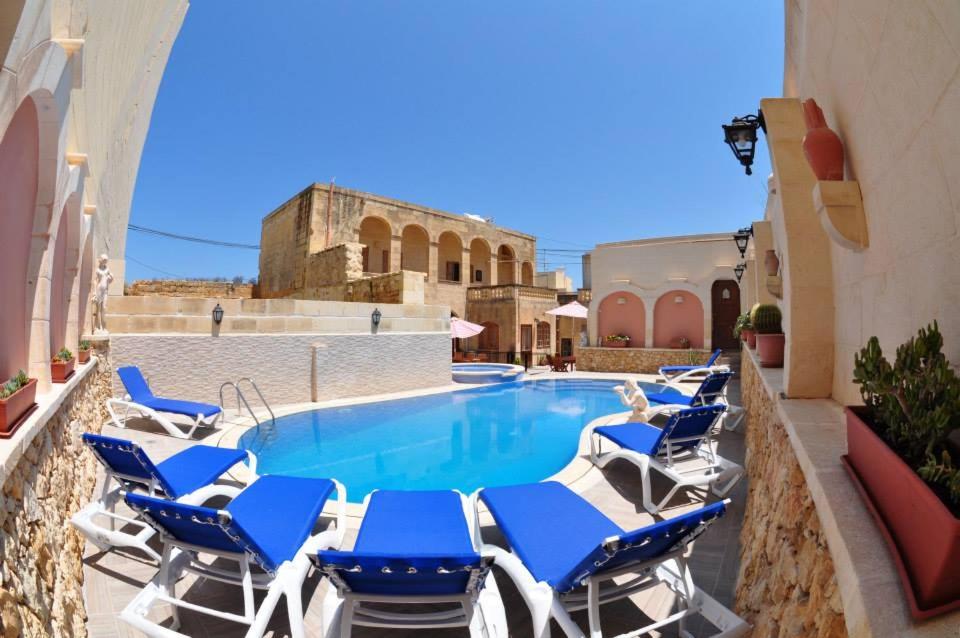 a pool with blue and white chairs next to a building at Mikiel u Rosa Holiday Farmhouse with Large Private Pool in Żebbuġ
